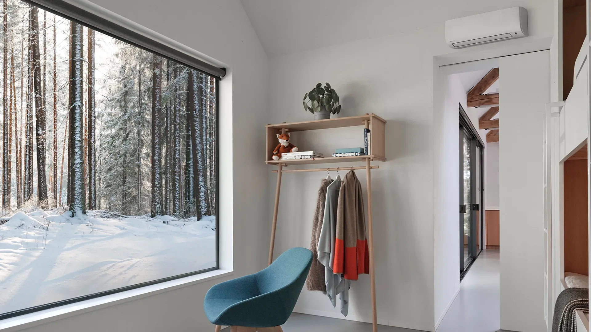 Luft-luft varmepumpe montert høyt på veggen i en lys stue med snødekt skog utenfor